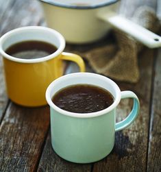 two mugs of coffee sitting on top of a wooden table next to each other