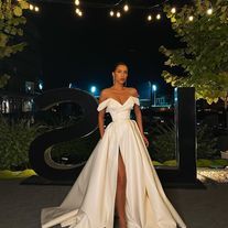 a woman standing in front of a sign wearing a white dress with high slits