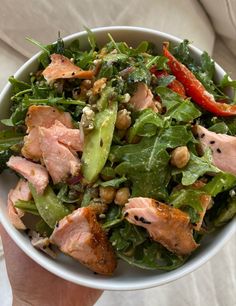 a person holding a white bowl filled with salad and meat on top of lettuce