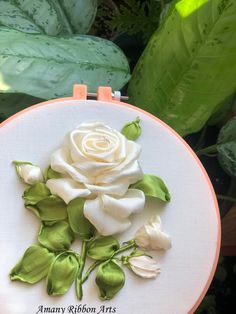 a white rose with green leaves is in a embroidery hoop