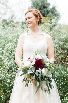 a woman in a wedding dress holding a bridal bouquet with red and white flowers