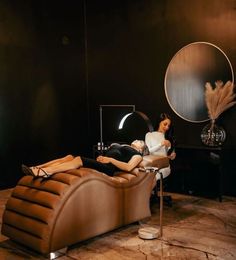 a woman laying on top of a brown chair next to a black table and mirror