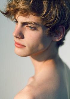 a young man with short hair and blue eyes stares into the distance while standing in front of a white background