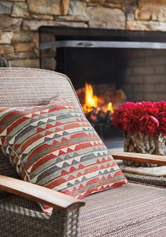 two wicker chairs sitting in front of a fire place with flowers on the table