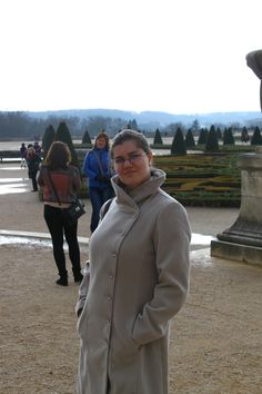 a woman standing in front of a fountain with people walking around her and looking at the camera