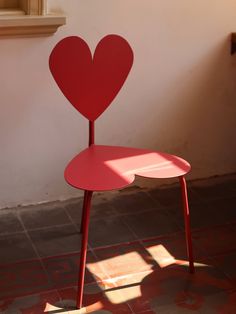 a red chair with a heart shaped seat on it's back in front of a window