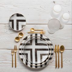 a table setting with black and white plates, gold cutlery and silverware on it