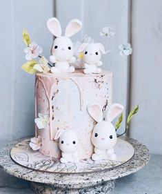 a pink cake with three bunnies on top and flowers in the middle, sitting on a marble pedestal