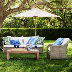 two wicker couches and an umbrella on the grass in front of some trees