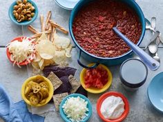 a table topped with bowls filled with chili and other toppings next to tortilla chips