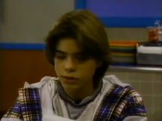 a young man sitting at a table with food in front of him and looking off to the side