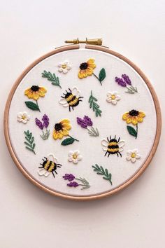 the embroidery is being worked on with flowers and bees in yellow, purple, and white