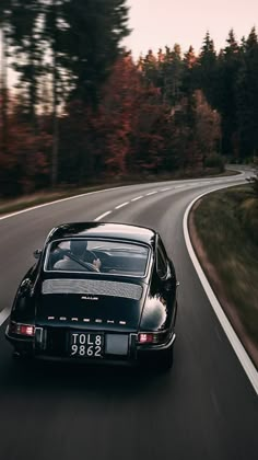 a black and white photo of a car driving down the road with trees in the background