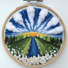 an embroidery art work with clouds and flowers in the center, on a white wall