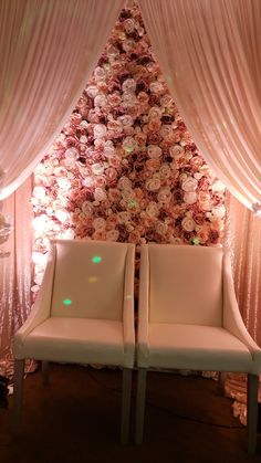 two white chairs sitting in front of a flower covered wall with pink flowers on it