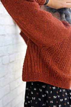 a woman wearing an orange sweater and black polka dot pants is holding her cell phone up to her ear