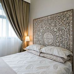 a white bed sitting under a window next to a lamp on a wooden headboard