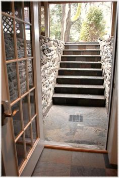 an open door leading to a set of stairs with stone walls and windows on either side