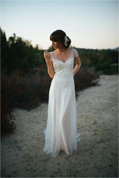 a woman in a white dress standing on a dirt road with her hand up to her face