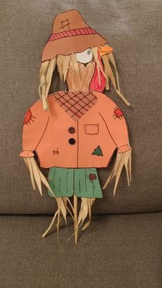 a paper cut out of a scarecrow wearing a hat and green pants on a couch