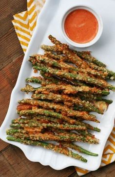 fried asparagus with dipping sauce on a white platter next to a yellow and white napkin