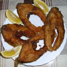 some fried food on a white plate with lemon wedges