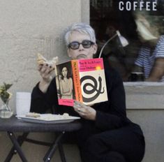 an older woman sitting at a table holding up a book