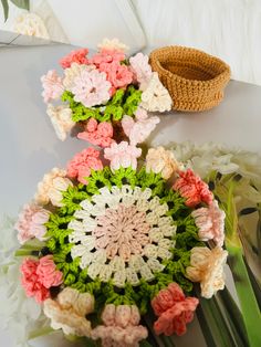 crocheted flowers are arranged on a white table with a basket in the background