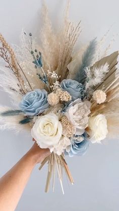 a person holding a bouquet with flowers and feathers on top of their head in front of a white wall