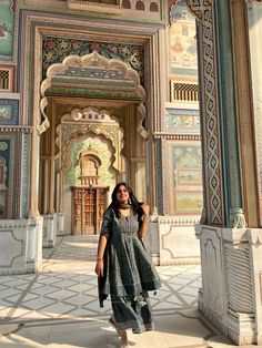 a woman standing in front of a building with intricately painted walls and arches,