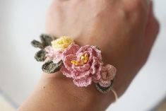 a woman's hand holding a crocheted bracelet with pink and yellow flowers