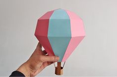 a hand holding an origami hot air balloon in pink, blue and green