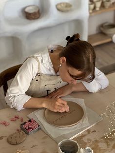 a woman in an apron working on a clay sculpture with other pottery items around her