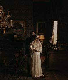 a man and woman standing next to each other in a dark room with chandelier