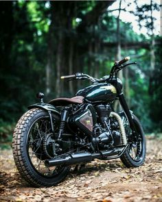 a black motorcycle parked on top of a leaf covered forest floor with trees in the background