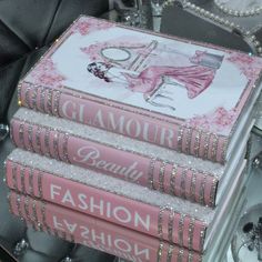 three books stacked on top of each other in front of a glass table with silver and pink decorations