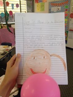 a child's hand holding up a piece of paper next to a pink balloon