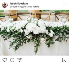 a table with white flowers and greenery is set up for an outdoor wedding reception