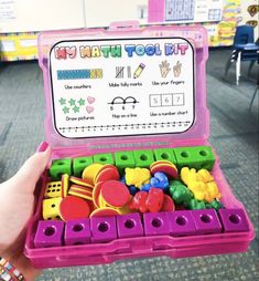 a child's hand holding a pink toy case filled with lots of colorful toys