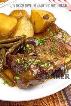 a white plate topped with meat and potatoes next to green beans on a wooden table