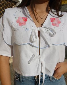 Tie front blouse in white with wide statement collar and floral embroidery. V neckline. Short sleeve. Ties to front. Size M/L, EU 38-44 / UK 10-16 Measurements: 40"/ 101cm bust - 10" / 25cm sleeve length - 17" / 43cm blouse length. Condition - New. Material - Cotton. Sustainability - Remade by our in house team using vintage fabrics. Model is a UK 6/8 & 5'7" tall. Statement Collar, Button Blouse, Tie Front Blouse, Sleeveless Jacket, Neutral Outfit, Tie Blouse, Front Tie Top, V Neckline