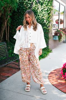 The Lakelyn Lace Ivory Button Up Top is a beautifully crafted, off-white lace and gauze blouse that exudes a romantic, bohemian vibe. The top features a delicate mix of lace and textured fabric, creating a soft and airy look perfect for layering. It has a button-down front with small, dark buttons that add a subtle contrast to the light fabric. The collar is slightly frayed, contributing to its relaxed and effortless style. The sleeves are voluminous and made entirely of intricate lace, adding a Spring Bohemian Crochet Lace Top, Cream Bohemian Lace Top For Spring, Spring Lace Trim Button-up Top, Bohemian Button-up Blouse For Vacation, Spring Button-up Lace Top With Lace Trim, Bohemian Cream Crochet Top For Day Out, White Flowy Breezy Blouse, Bohemian Button-up Blouse For Day Out, Bohemian Lace Blouse With Floral Embroidery