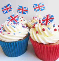 two cupcakes with white frosting and british flags on top, sitting next to each other