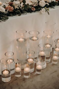 candles are lined up on a table with flowers and greenery