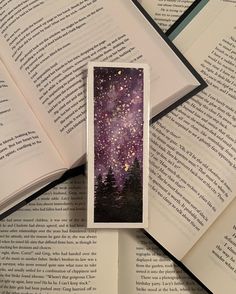 an open book on top of some books with stars in the sky and trees around it