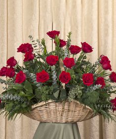 a basket filled with lots of red roses sitting on top of a table next to a curtain