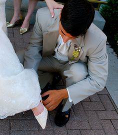 a man in a suit tying his shoes on the ground next to a woman in a wedding dress