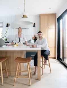 two people sitting at a kitchen island in the middle of a room with white walls