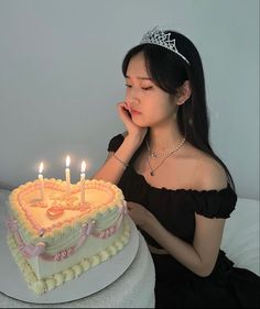 a woman sitting in front of a cake with lit candles on it and wearing a tiara