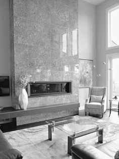 black and white photograph of living room with large stone fireplace in the center, couches and coffee table